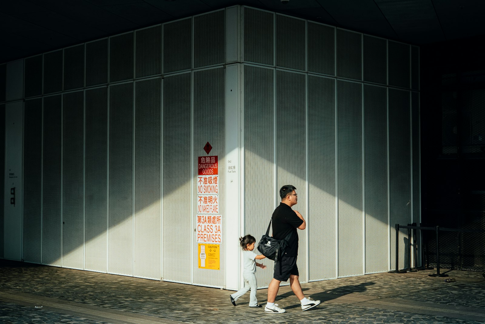A father and child walking together past a building in an Asian city