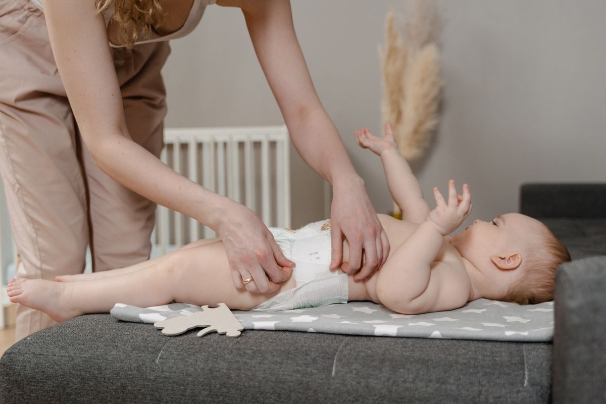 A parent gently changing a baby's diaper on a soft mat