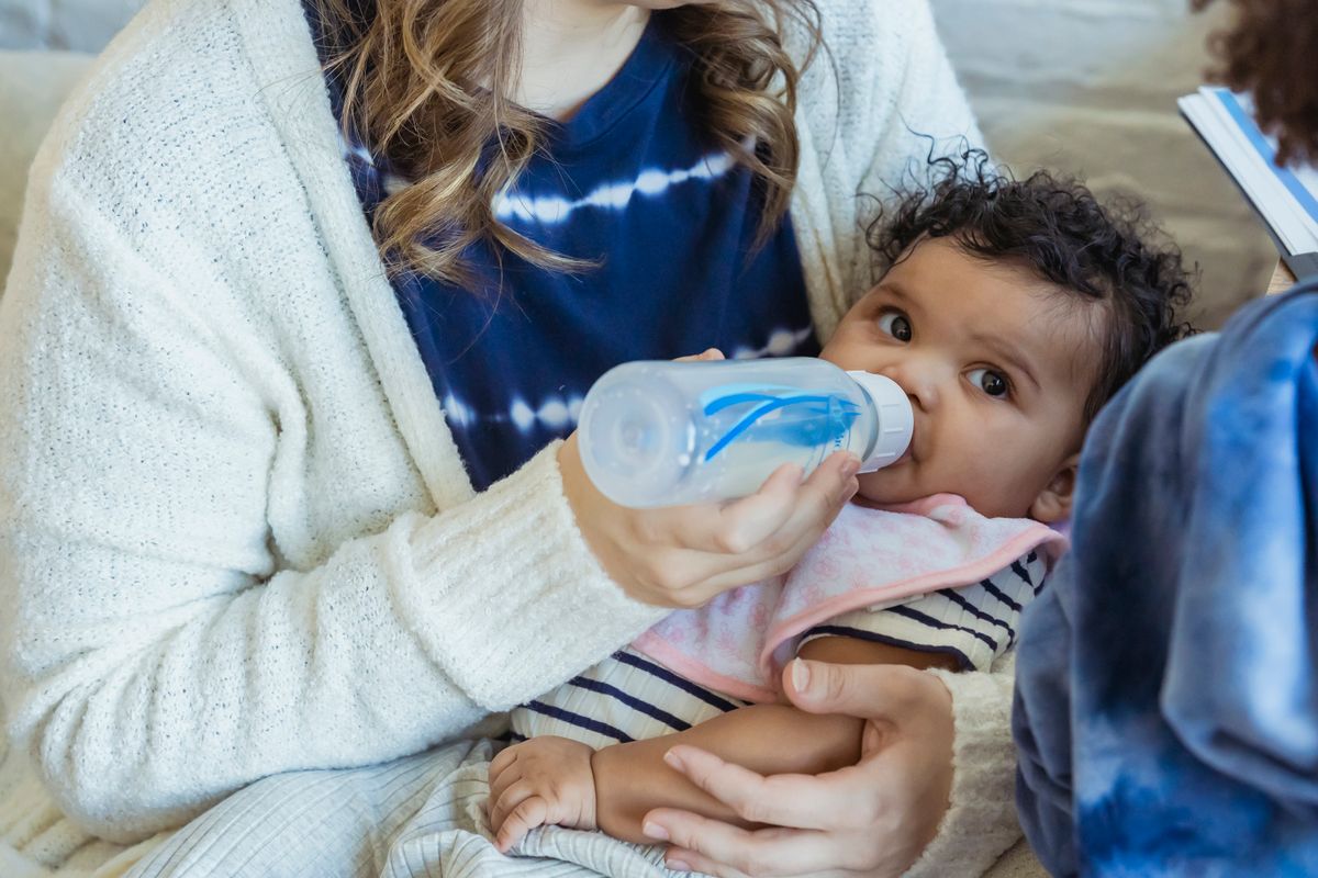 A mother bottle-feeding her baby, who is drinking eagerly