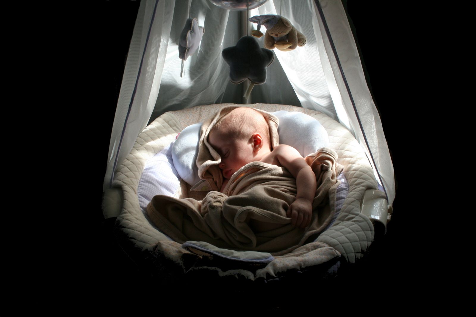A swaddled baby sleeping peacefully in a crib beneath a hanging star mobile