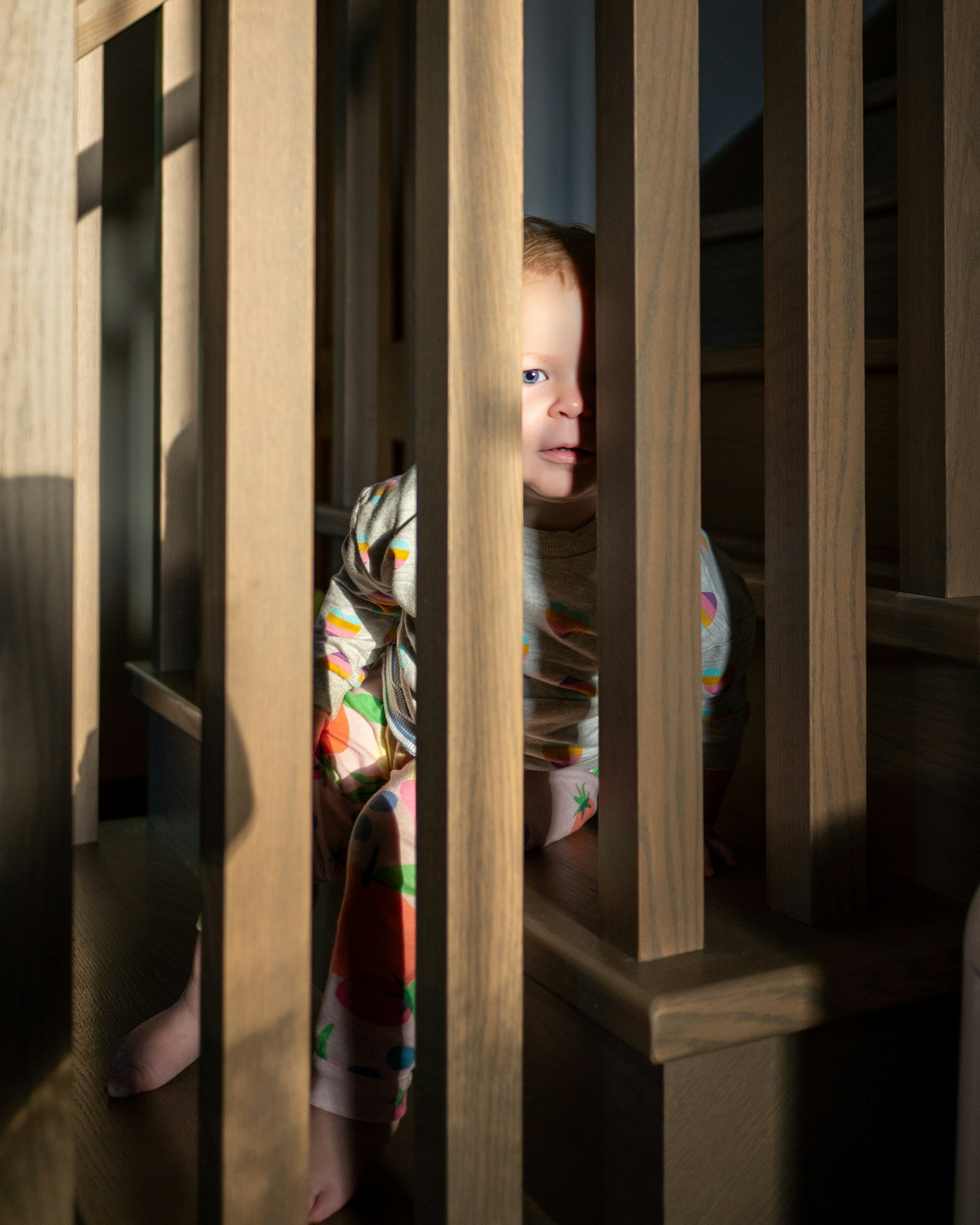A toddler peeks through wooden stair railings