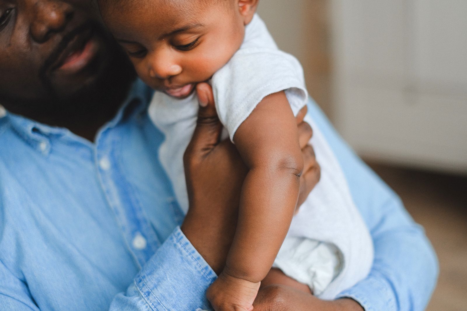 A father gently holds his baby upright against his shoulder while burping him after a feed