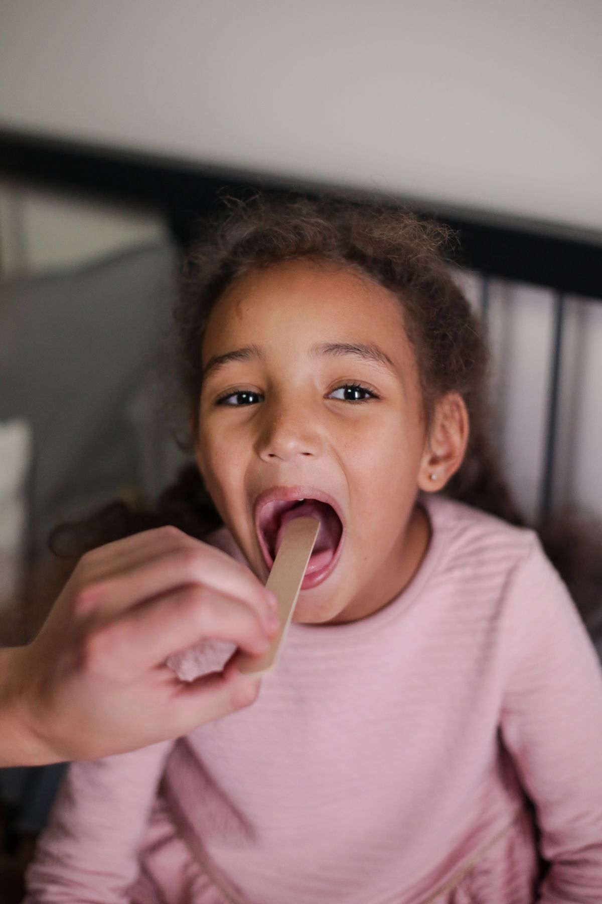 A young girl opening her mouth for a throat check at home