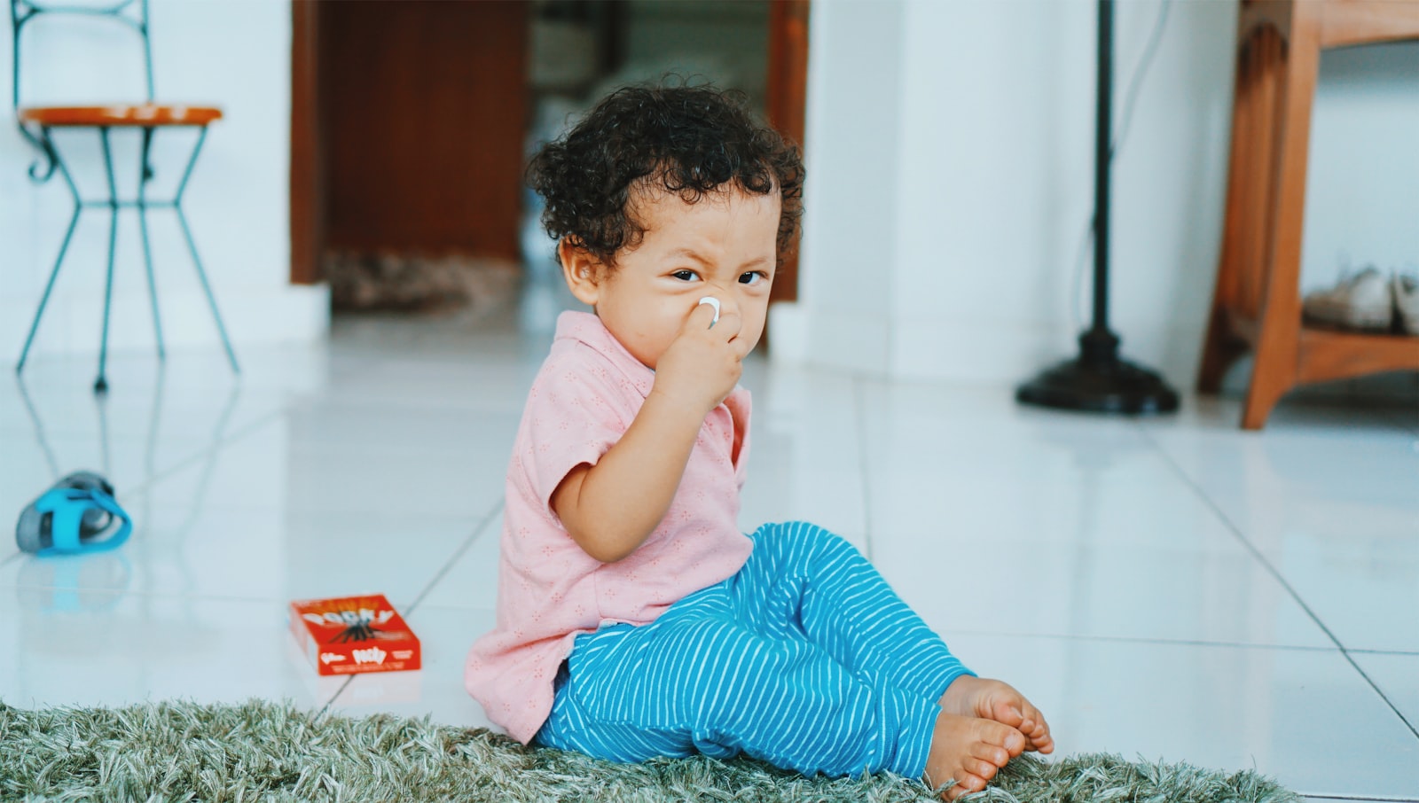A young child sitting on the floor holding a tissue near their nose
