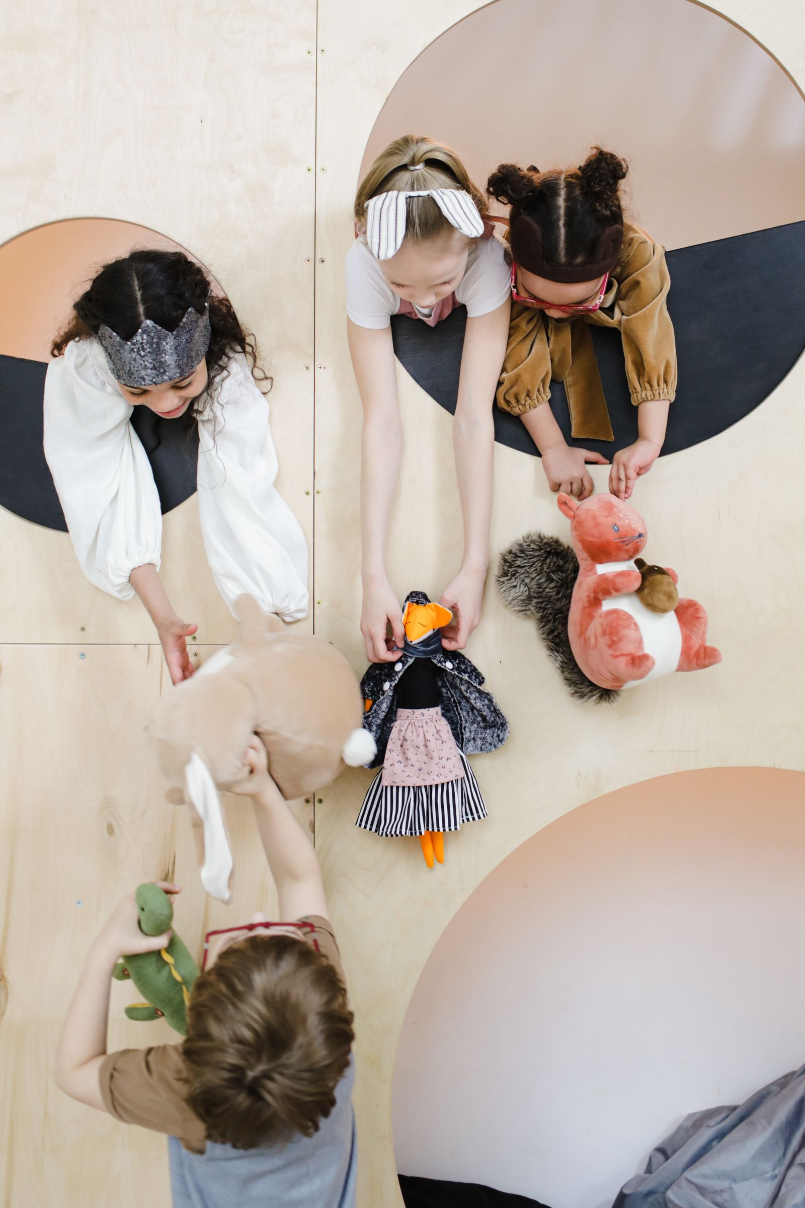 Four young children gathered on the floor together, taking turns holding stuffed animal toys