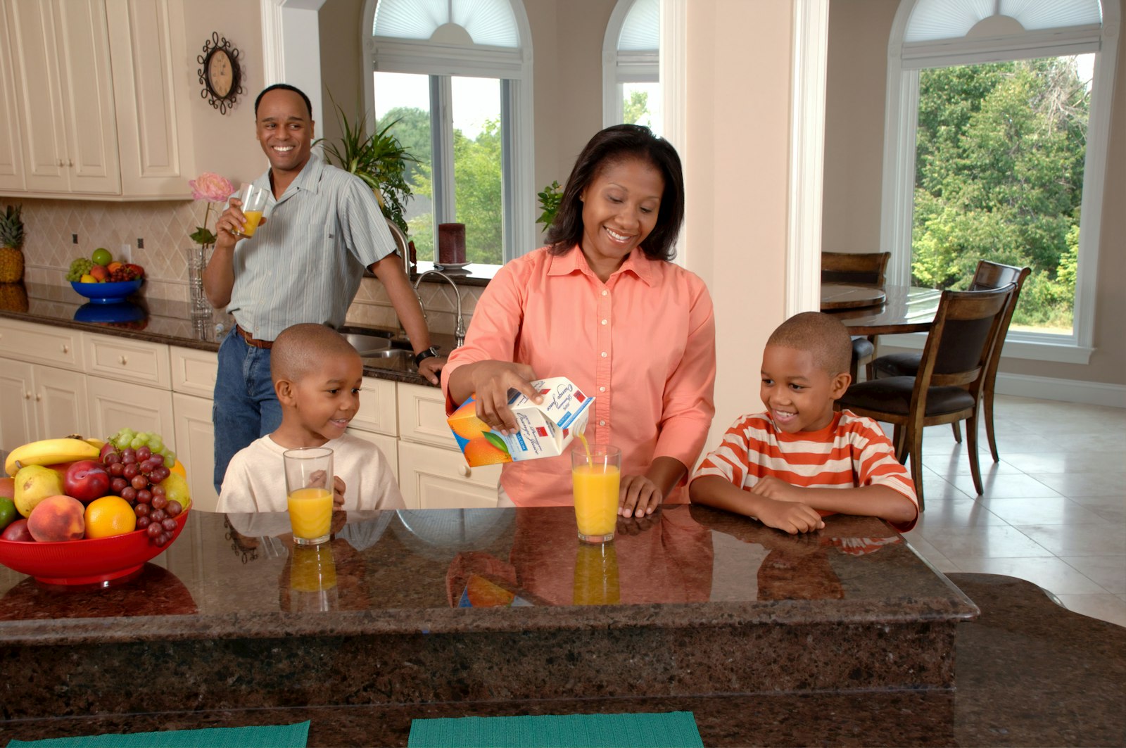 A family in the kitchen with two boys drinking from cups at the counter