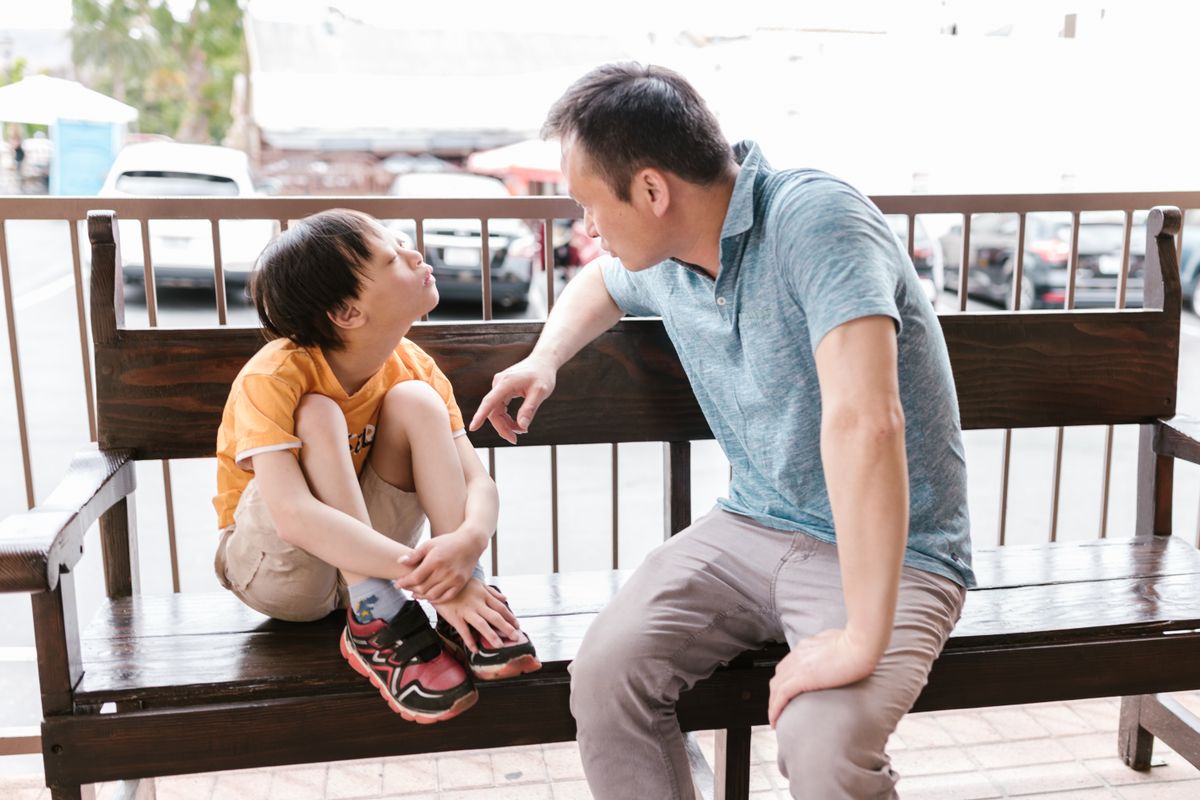A father sitting side by side with his son on a bench, having a gentle conversation