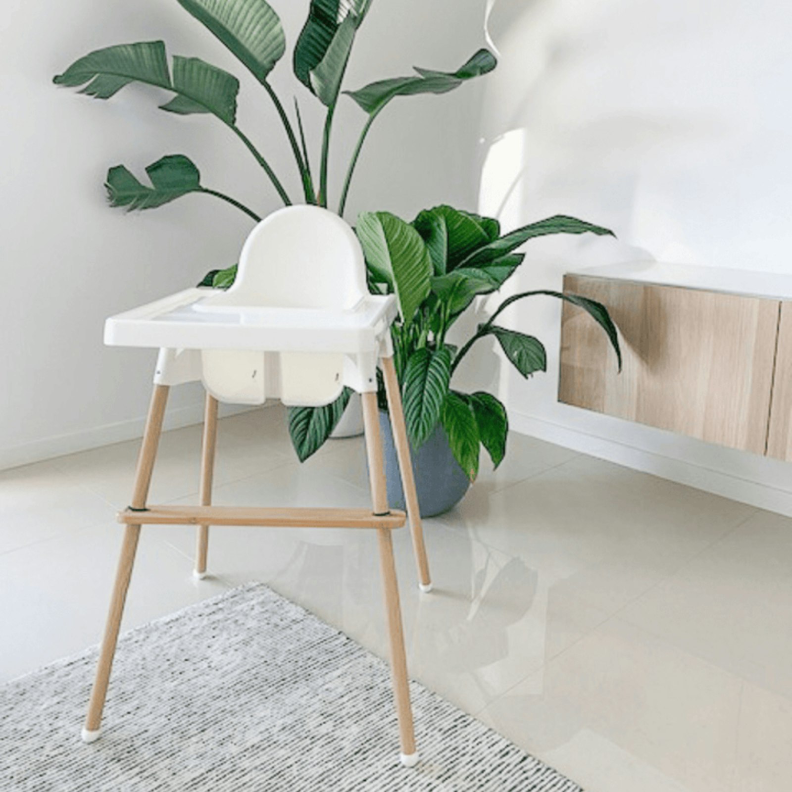 A modern wooden and white high chair standing next to a large plant