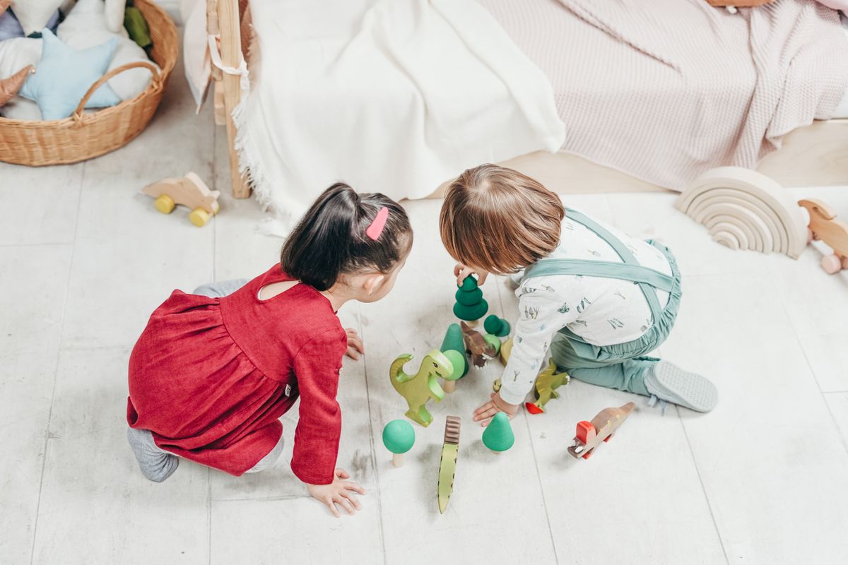 Two toddlers happily playing together with wooden toys on the floor