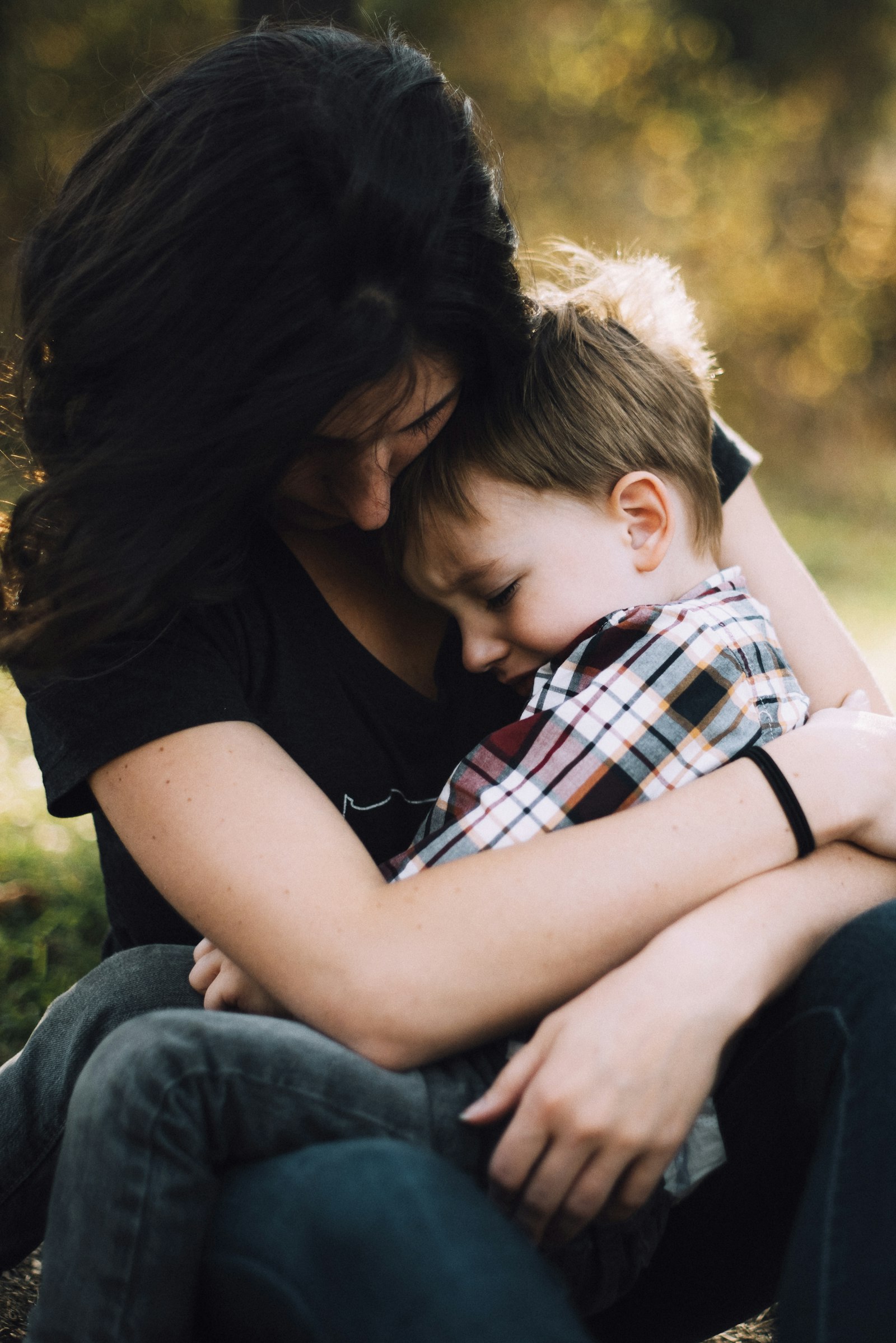 A mother gently comforting her young son with a warm embrace outdoors