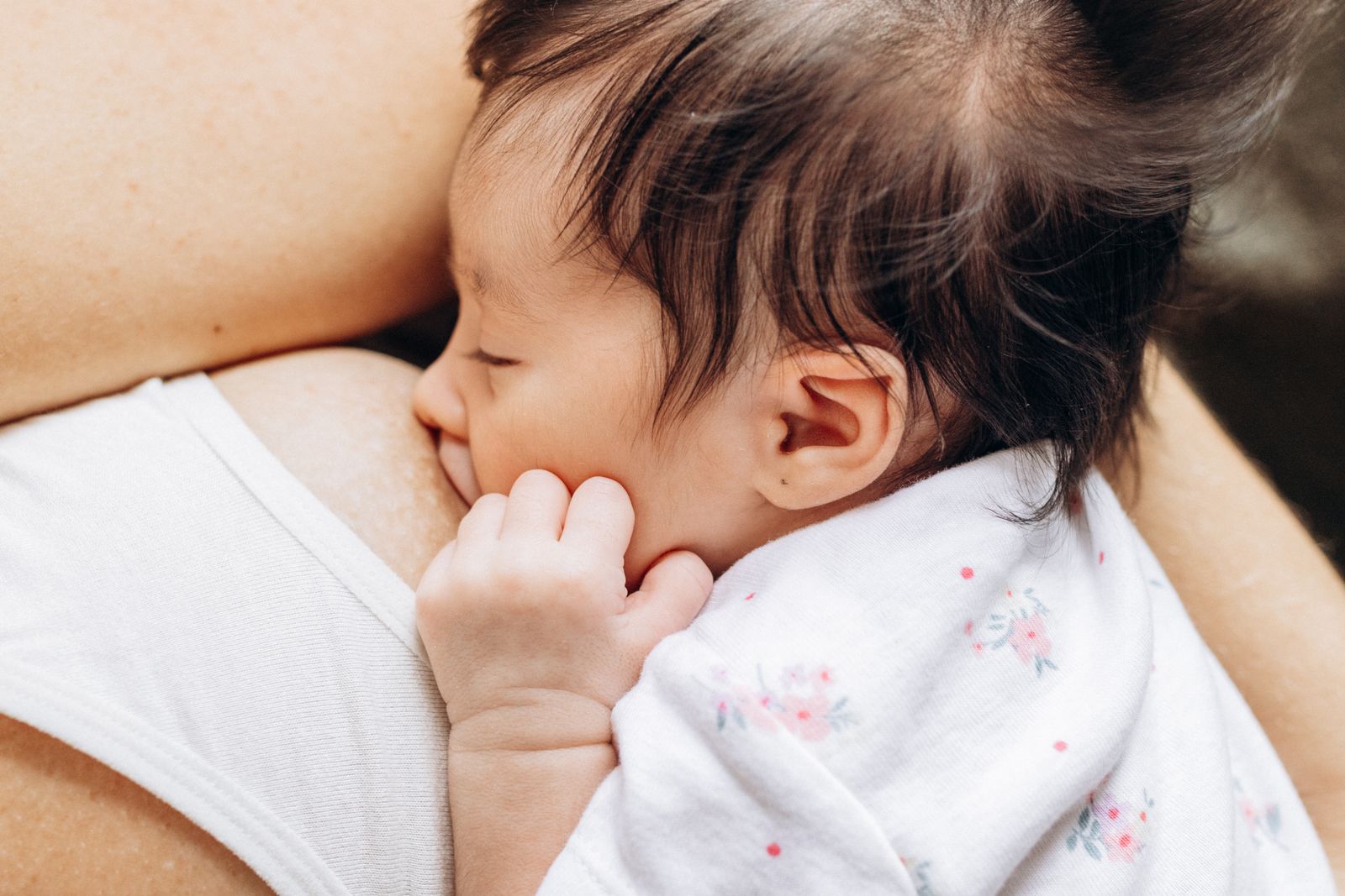 Close-up of a newborn breastfeeding against the mother's chest, latched deeply with a visible wide-open mouth