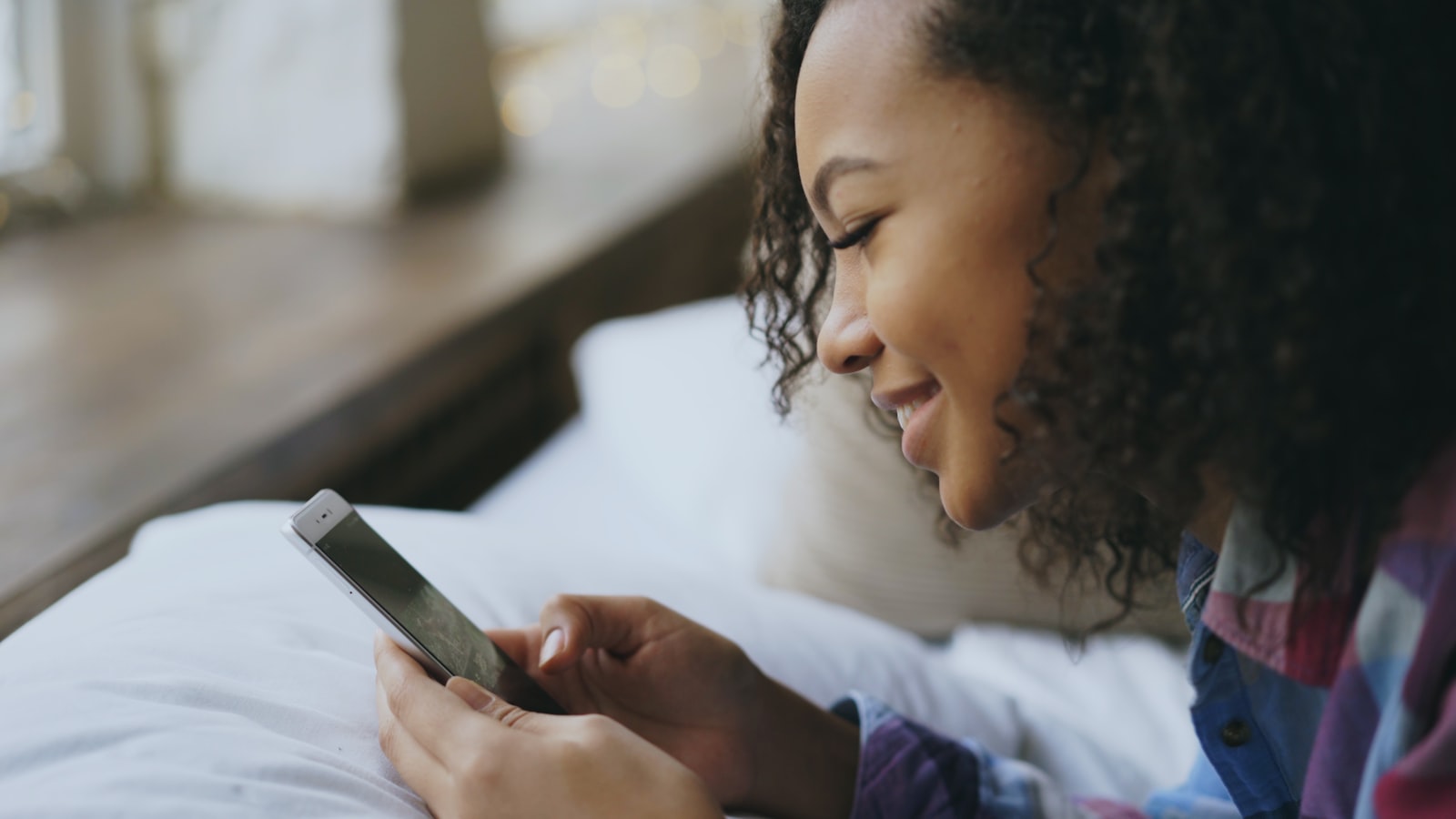 Young woman smiling while checking her phone in bed