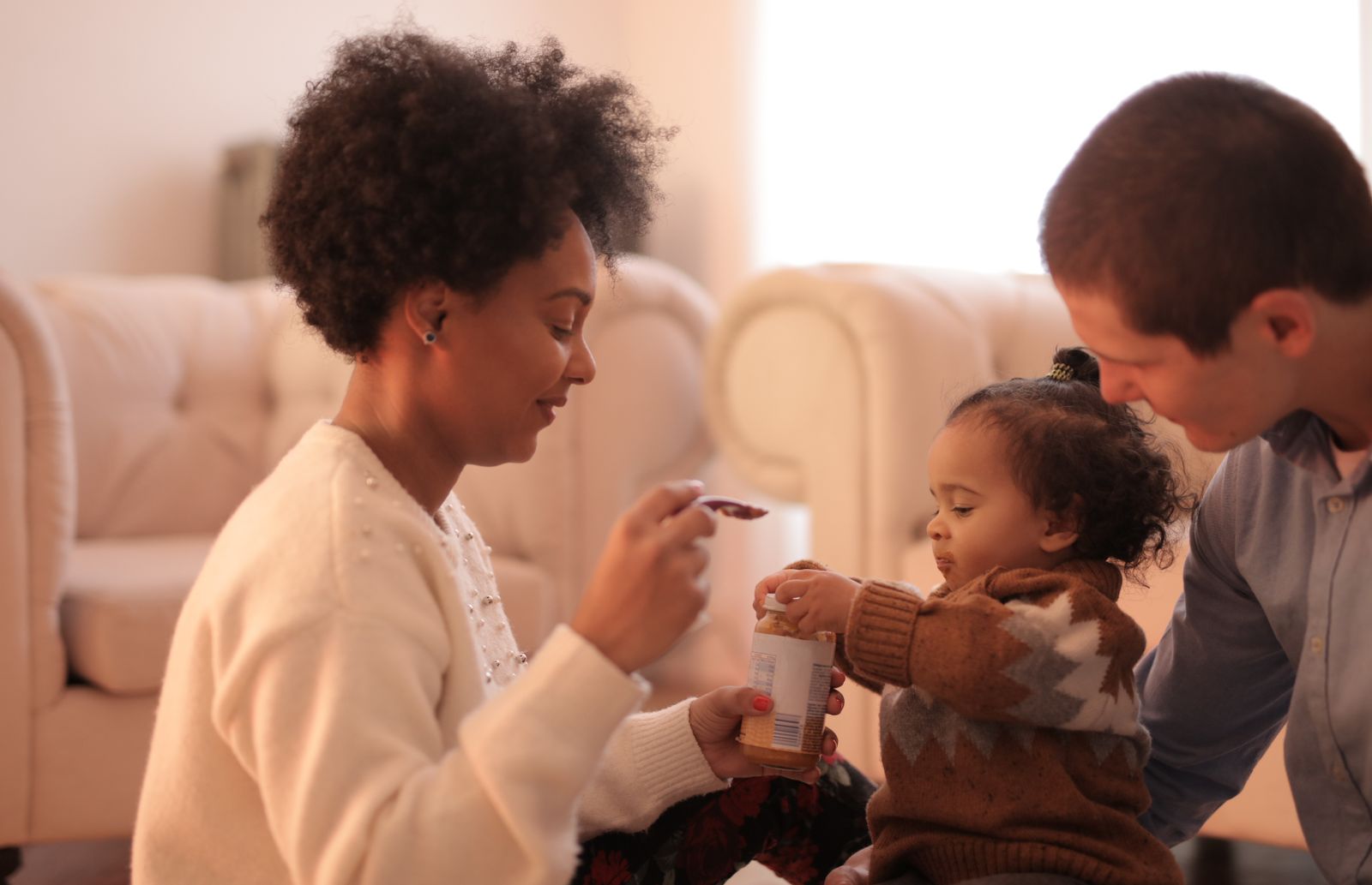 A parent feeding a toddler with a spoon while sitting close together at home