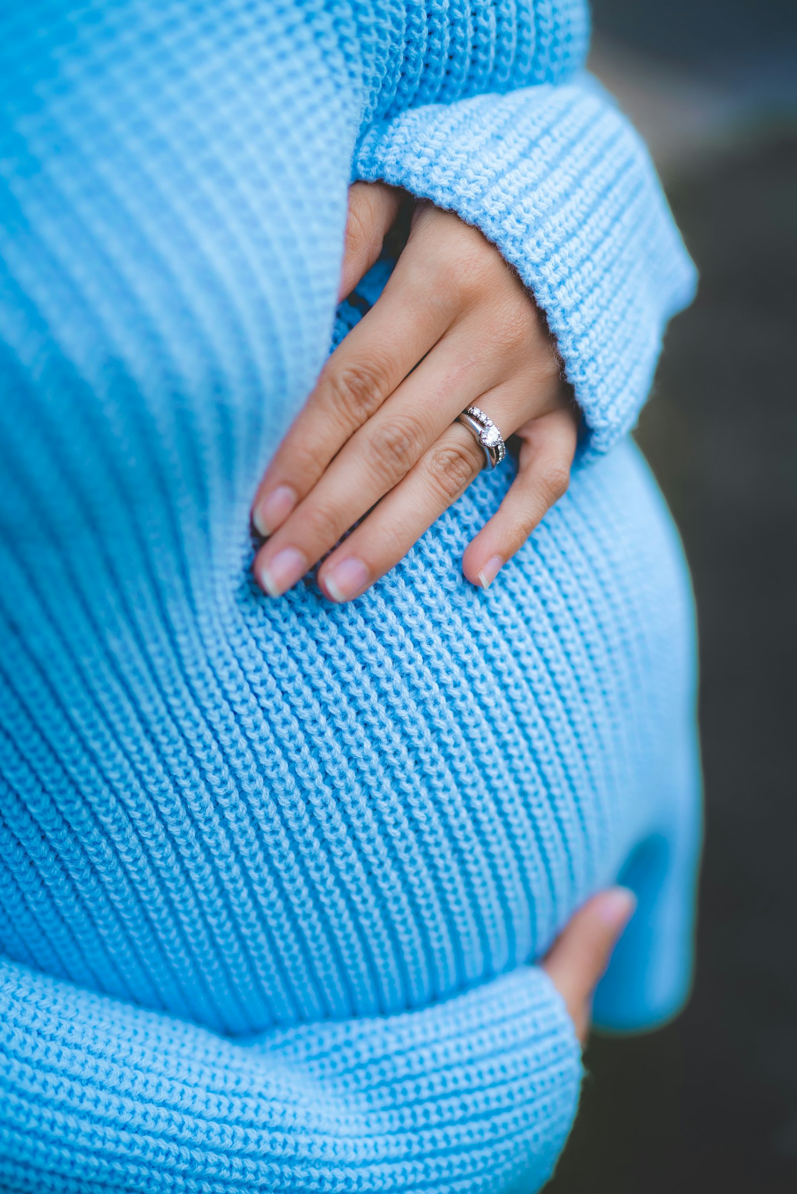 A woman holding her pregnant belly, wearing a blue knit sweater