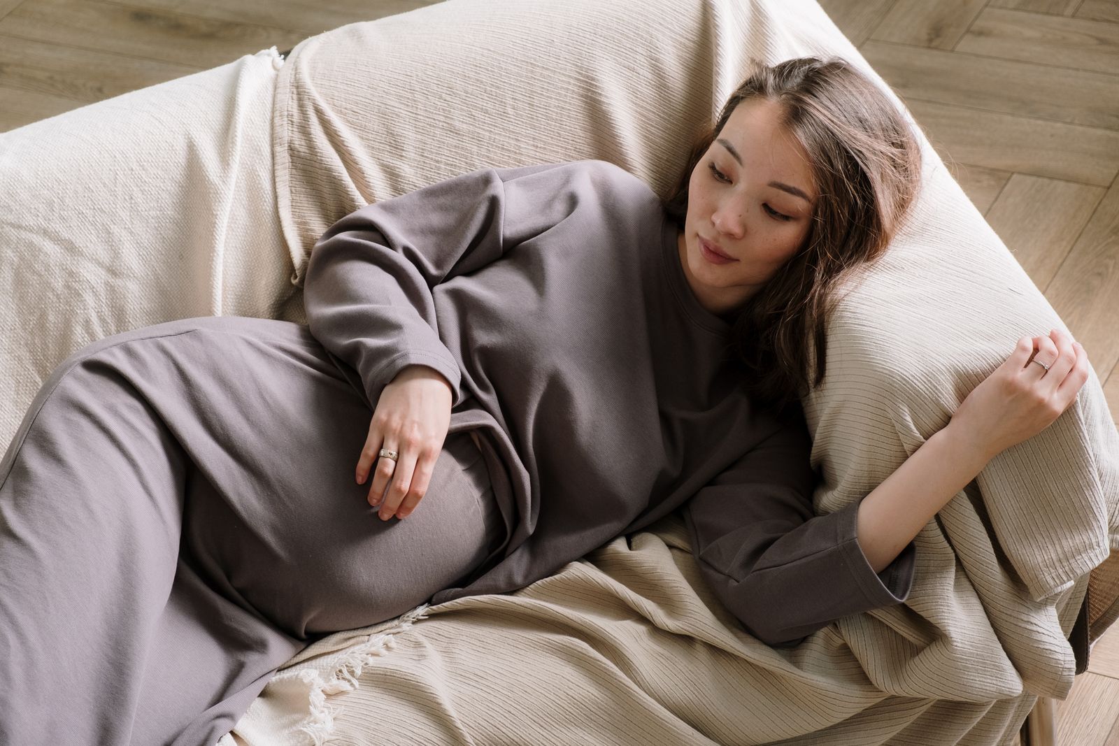 A pregnant woman resting on a cream sofa, lying back with her legs stretched out and one hand on her belly