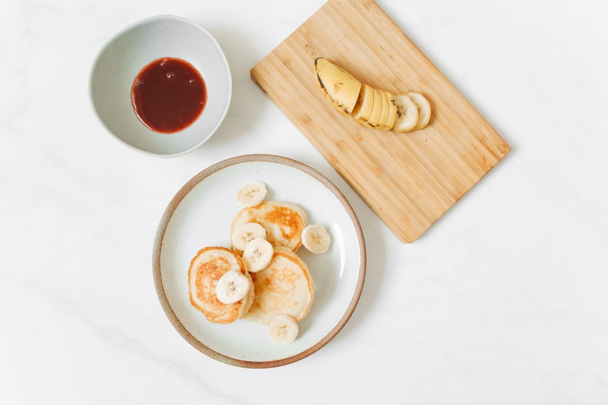 A small stack of banana pancakes topped with banana slices on a white plate
