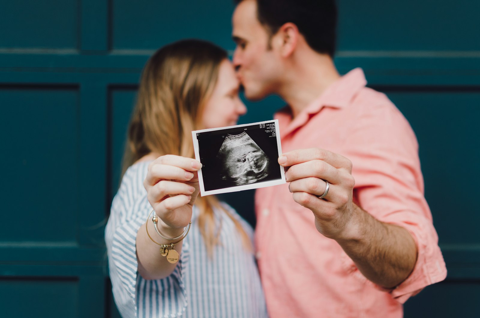 Man kissing woman's forehead while she holds an ultrasound photo