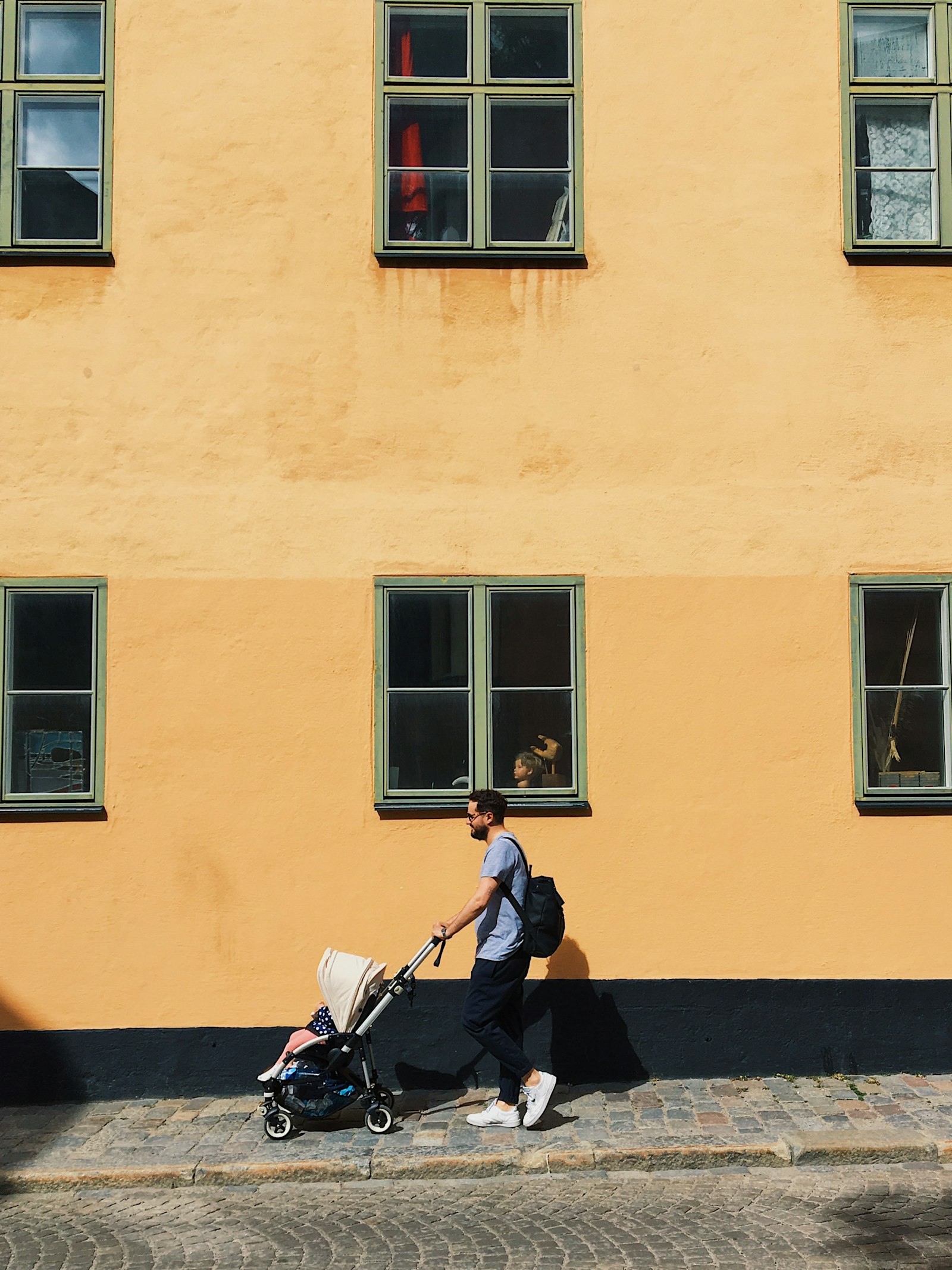 A father pushing a stroller past a colorful building on a city sidewalk