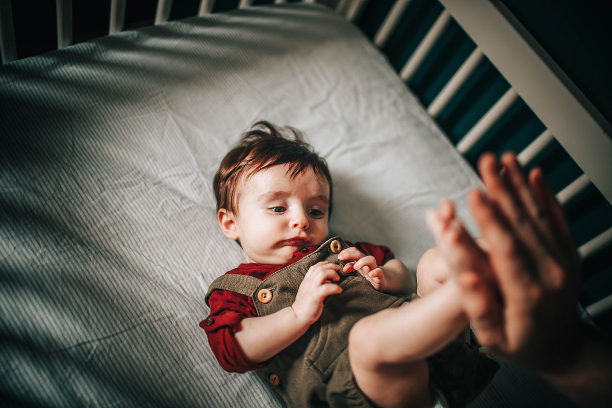 A wide-awake toddler in a crib during what should be naptime, with a parent's hand reaching in