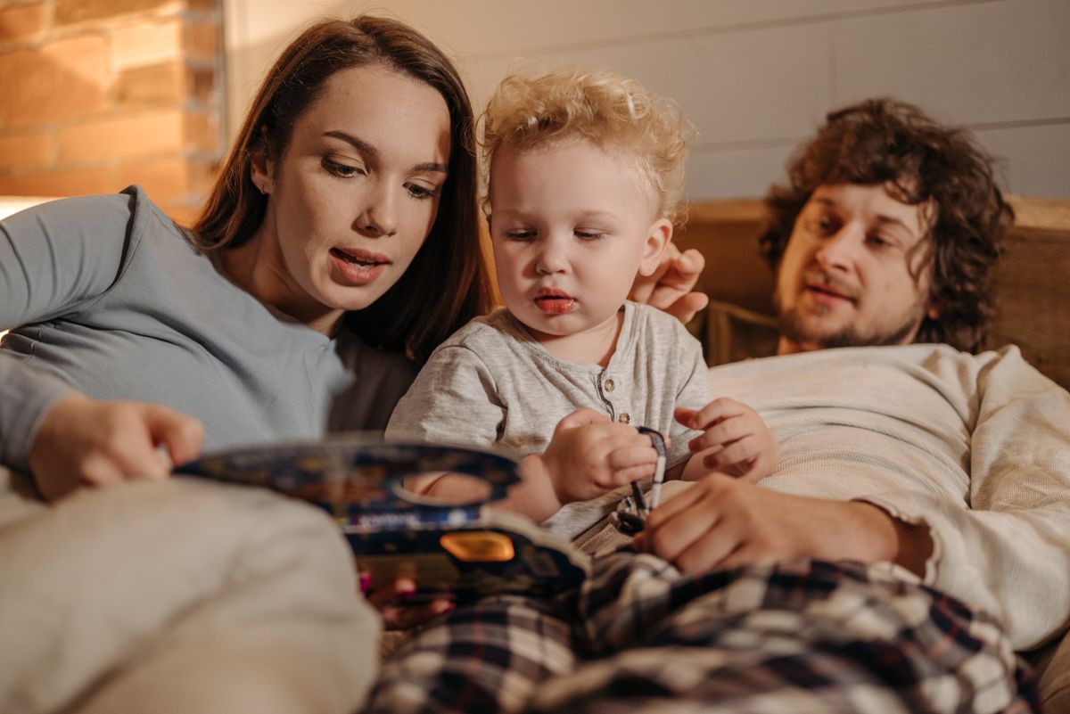Two parents reading a bedtime story to their toddler in bed