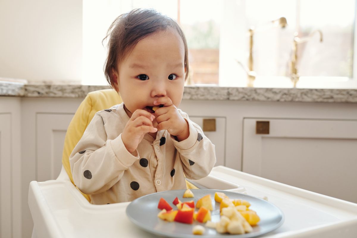 A toddler enjoying fresh fruit pieces in a high chair