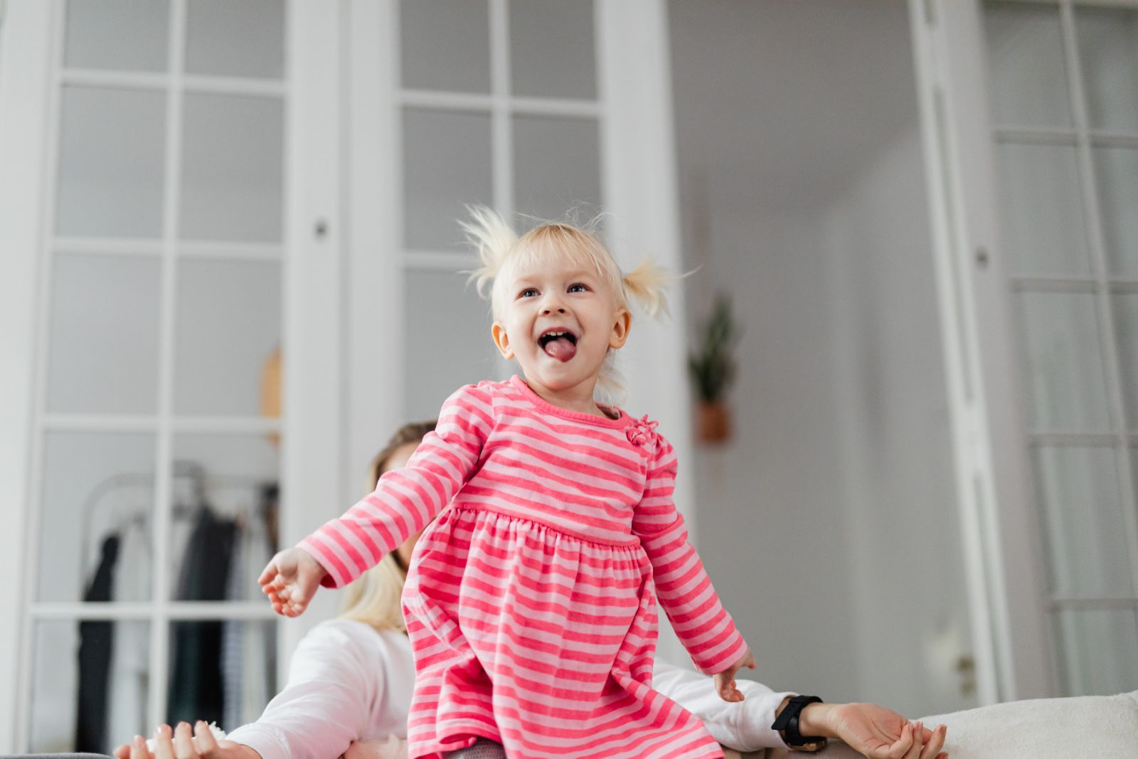 Toddler in a striped dress jumping and laughing indoors