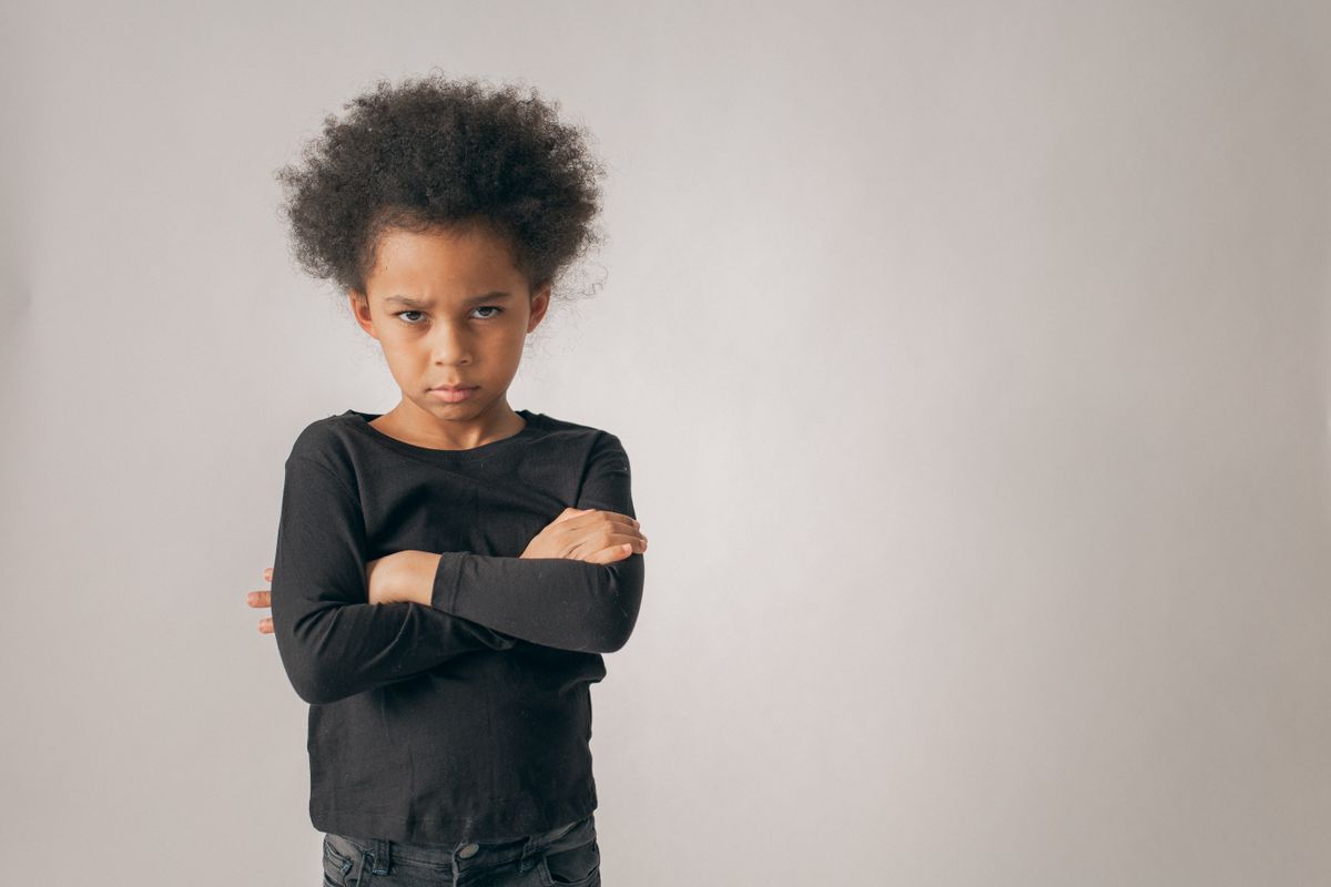 A young child standing with arms crossed, looking defiant
