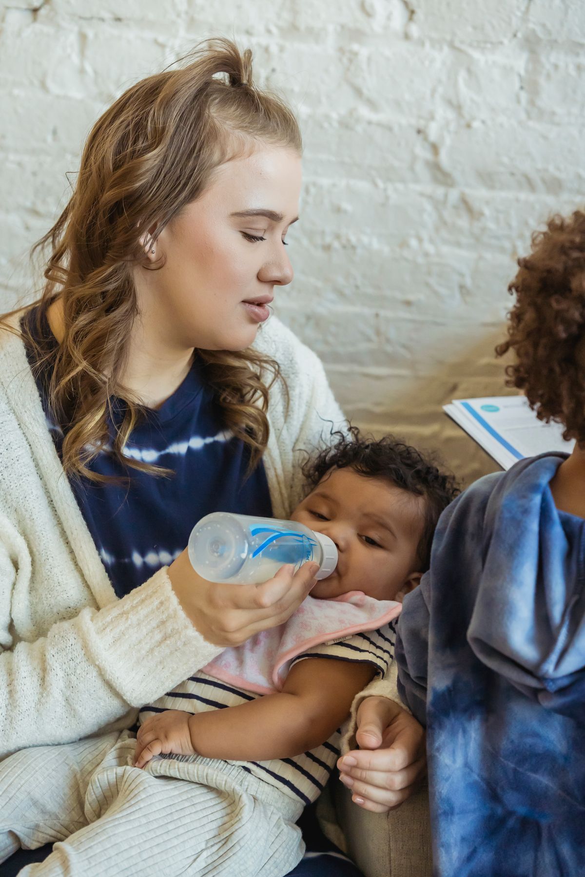 A mother bottle-feeding her baby while sitting with her other child